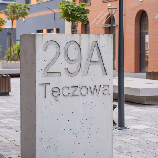 Betonowy blok z numerem 29A przy ulicy Tęczowej na tle nowoczesnych budynków