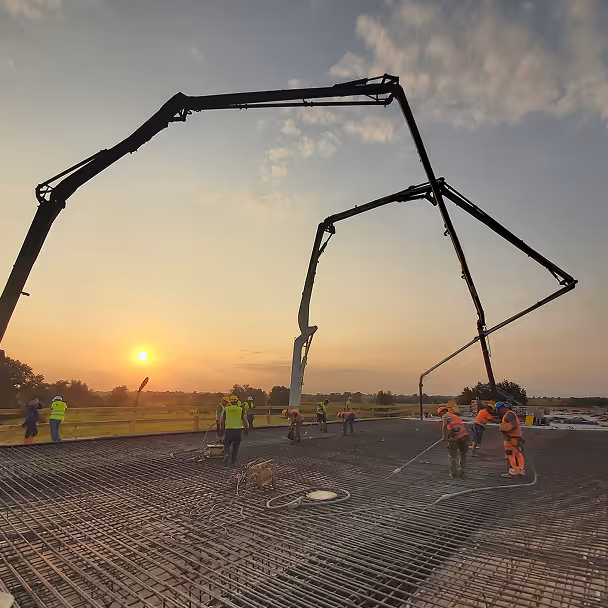 Pracownicy budowlani wylewają beton na zbrojenie płyty konstrukcyjnej o zachodzie słońca