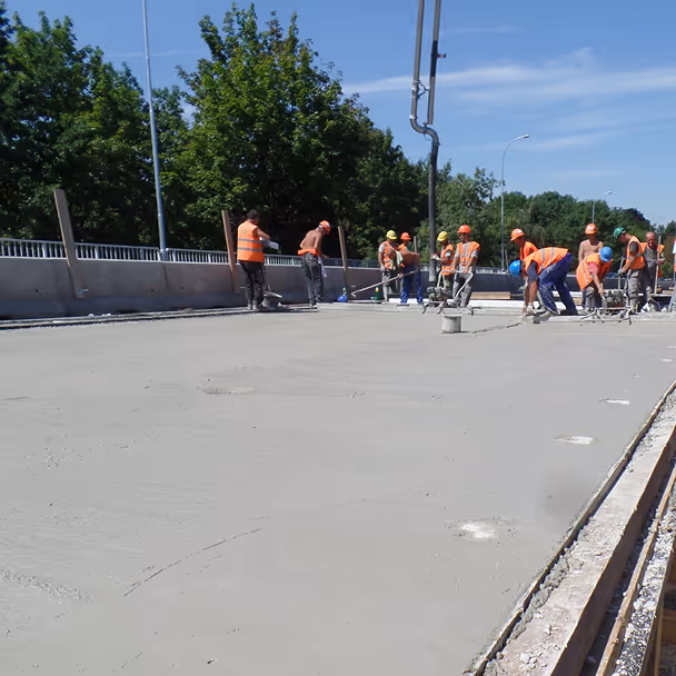 Robotnicy wyrównują świeżo wylany beton na placu budowy mostu