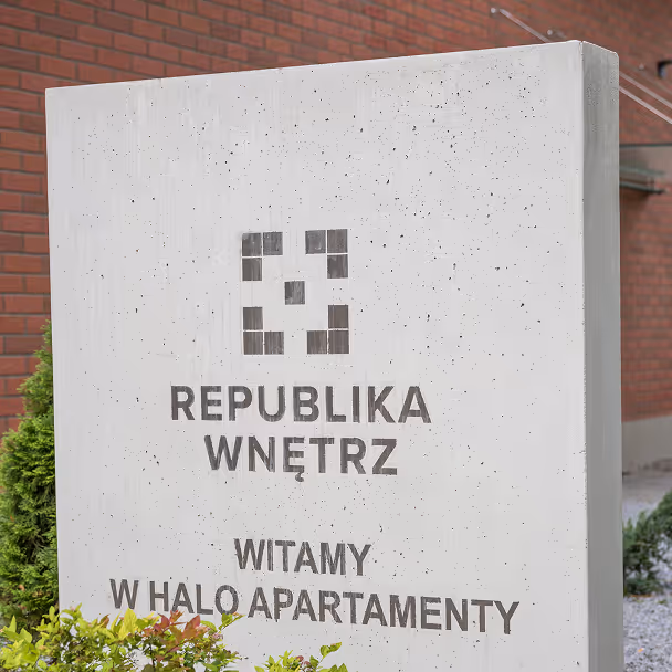 Betonowy pylon z napisem Republika Wnętrz przed budynkiem mieszkalnym