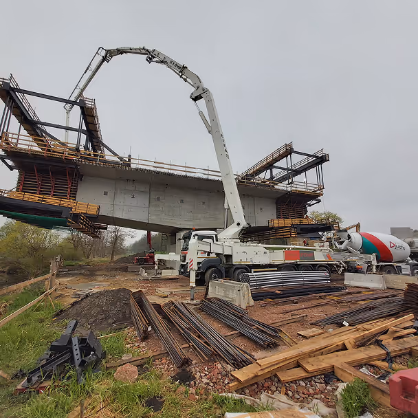 Samochód pompowy wylewa beton na budowę mostu, pręty zbrojeniowe na placu