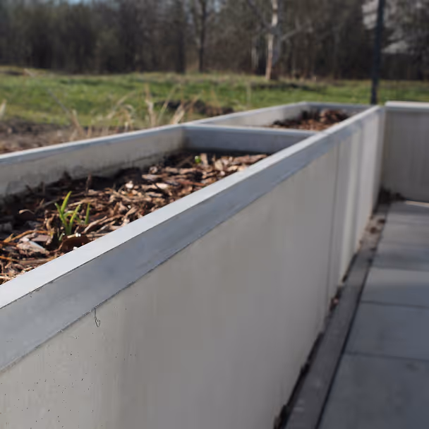 Betonowa donica w ogrodzie z rosnącymi roślinami, idealna dla architektury krajobrazu