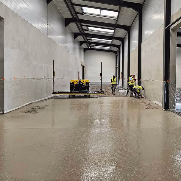 Pracownicy budowlani poziomują betonową posadzkę w hali przemysłowej