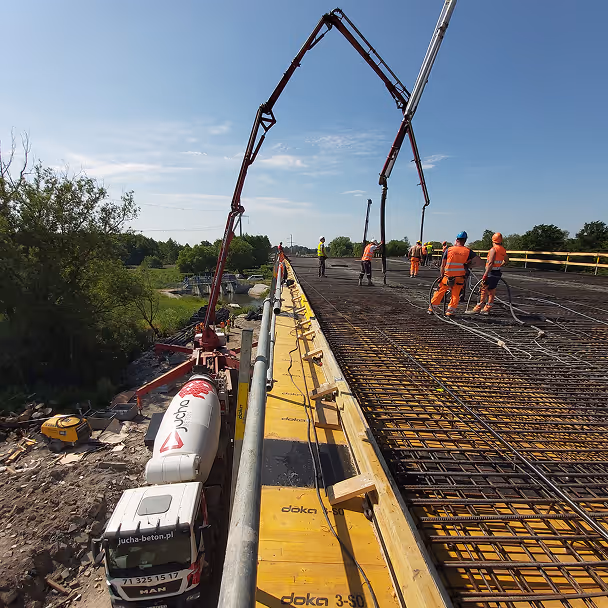 Robotnicy budowlani wylewający beton na konstrukcję mostu przy użyciu pompy betonowej