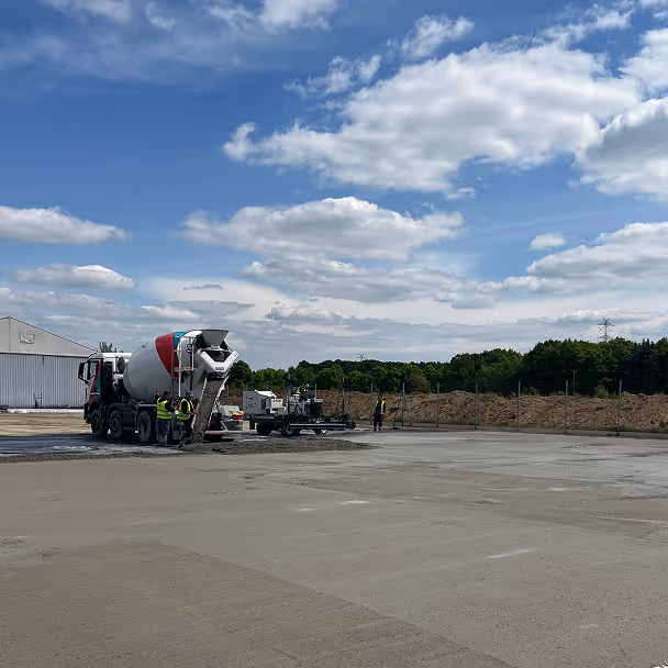 Betoniarka wylewająca beton na placu budowy z pracownikami w tle