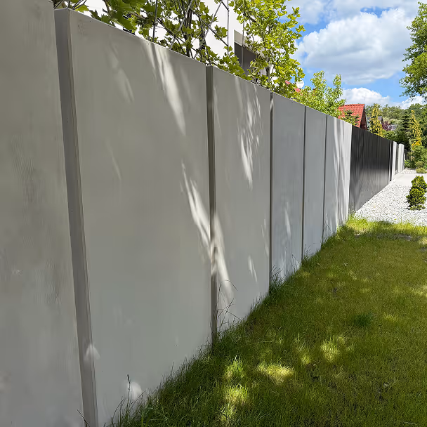 Nowoczesny betonowy mur ogrodzeniowy przy zielonym trawniku, słoneczny dzień