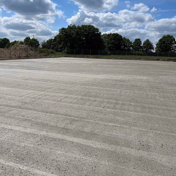 Świeżo wylany plac betonowy na placu budowy otoczony zielenią