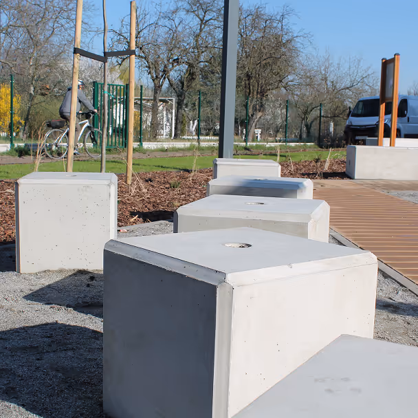Betonowe bloki używane jako siedziska w parku z alejką w tle
