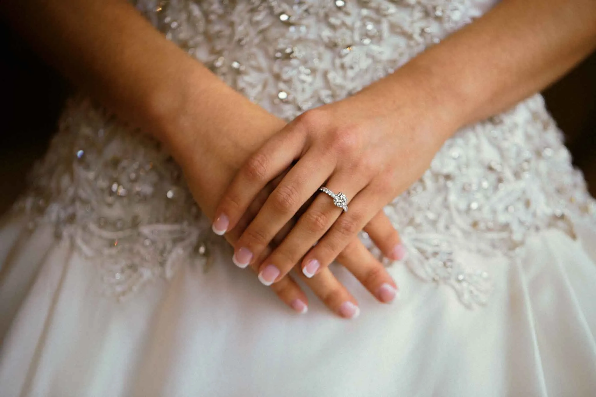 Close-up of a bride’s hands resting gently on her beaded wedding dress, showcasing a diamond ring, captured in the timeless style of analog wedding photography NJ.