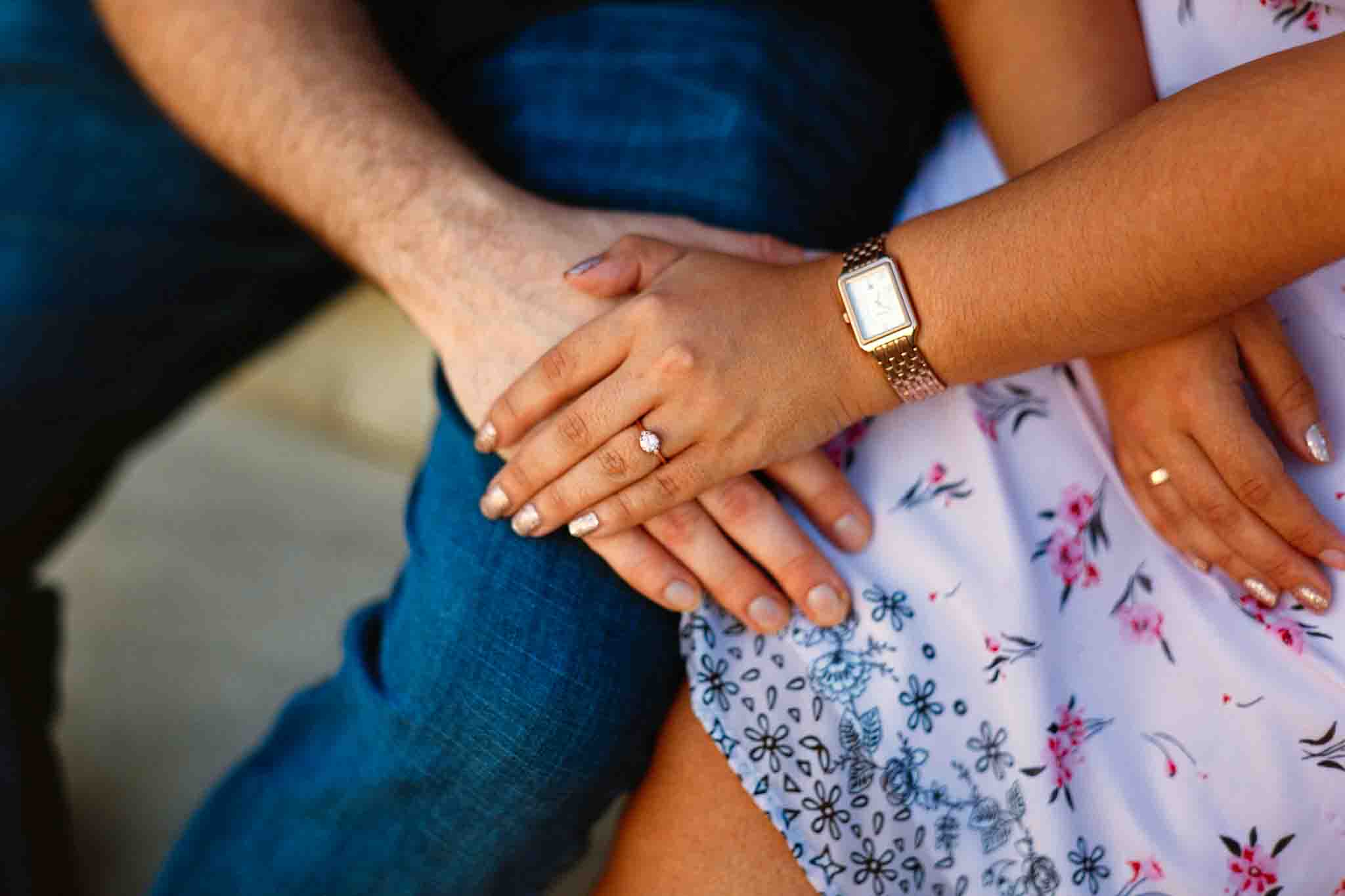 A close-up of two people sitting side by side, gently holding hands. One hand displays an engagement ring and a gold watch. Captured by a candid film wedding photographer NJ, the scene radiates intimacy and affection in casual, heartfelt style.