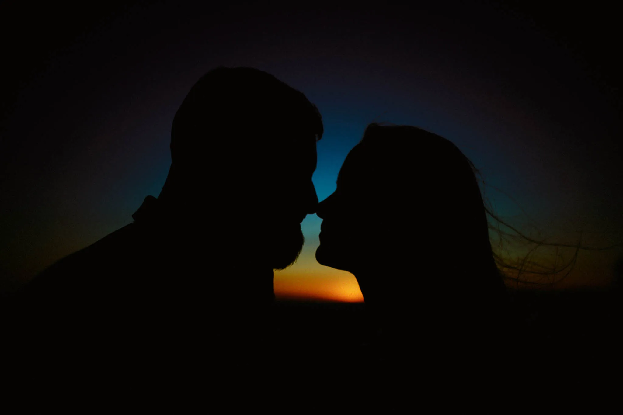 Silhouette of two people facing each other closely at sunset, with a gradient sky transitioning from deep blue to orange—captured in the timeless style of a New Jersey film wedding photography session.