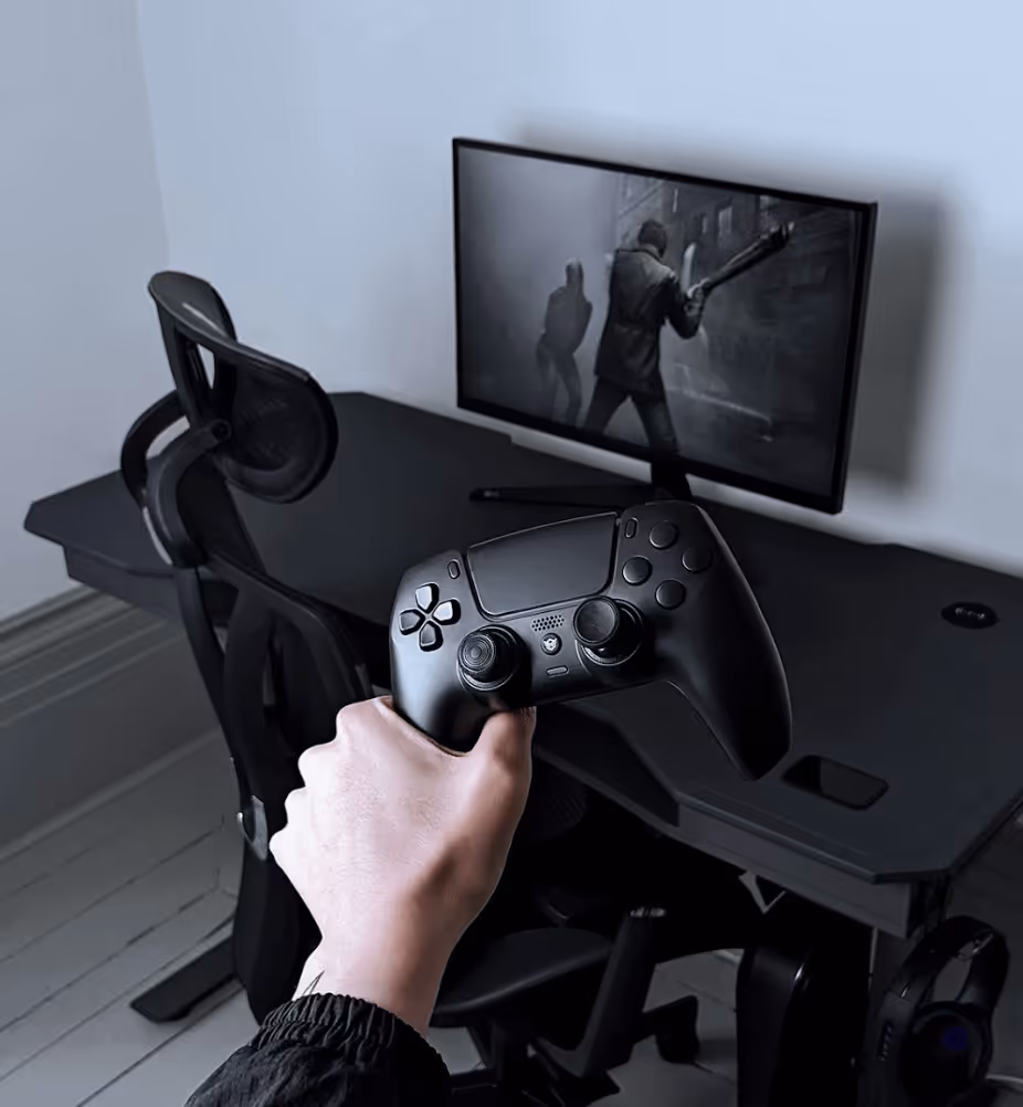 Hand holding pPlaystation controller with the Cyclone gaming desk setup in the background