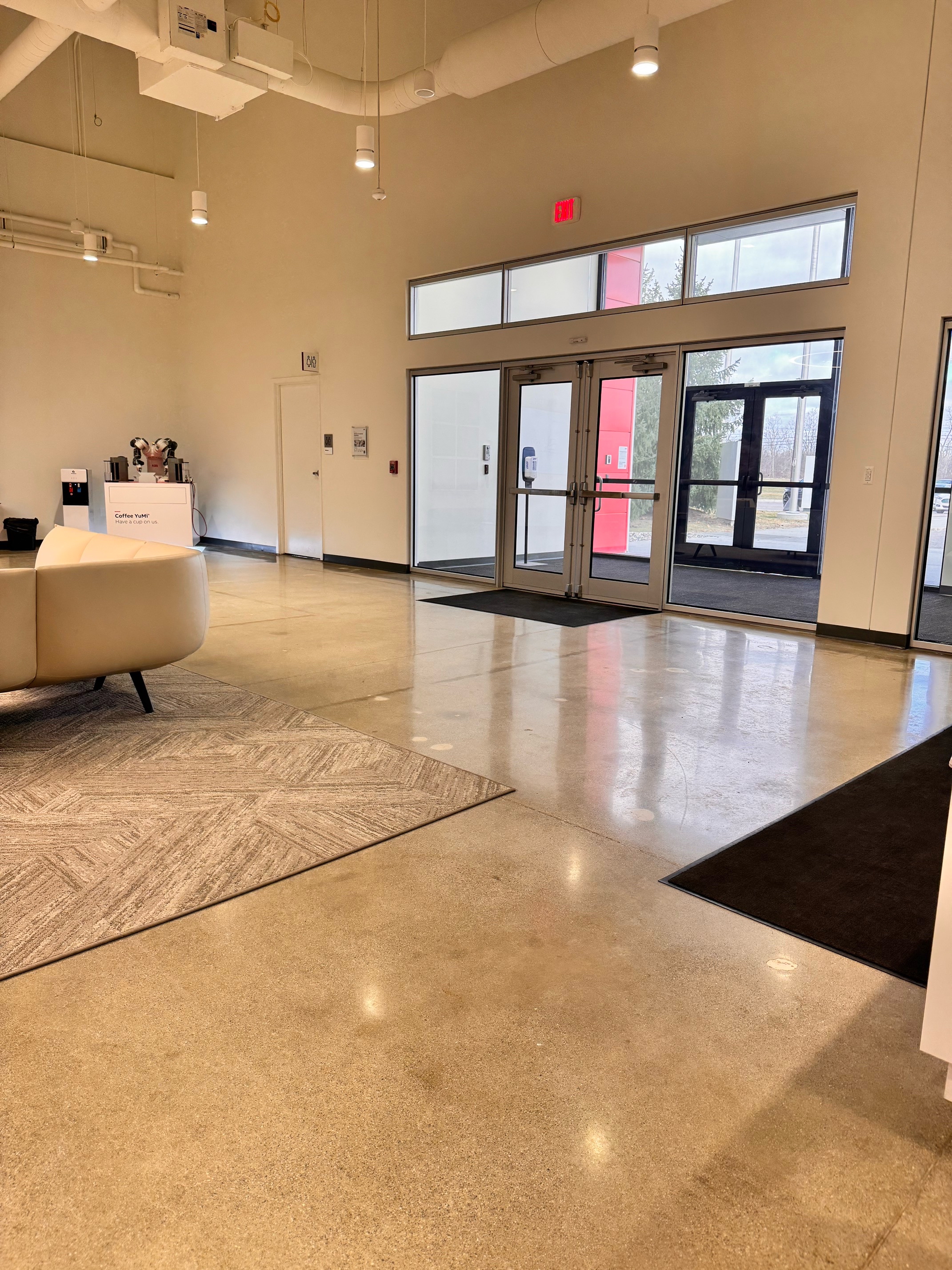 Modern conference room with a long wooden table, eight mesh office chairs, a digital phone, remote controls, and a large landscape photo on the wall.