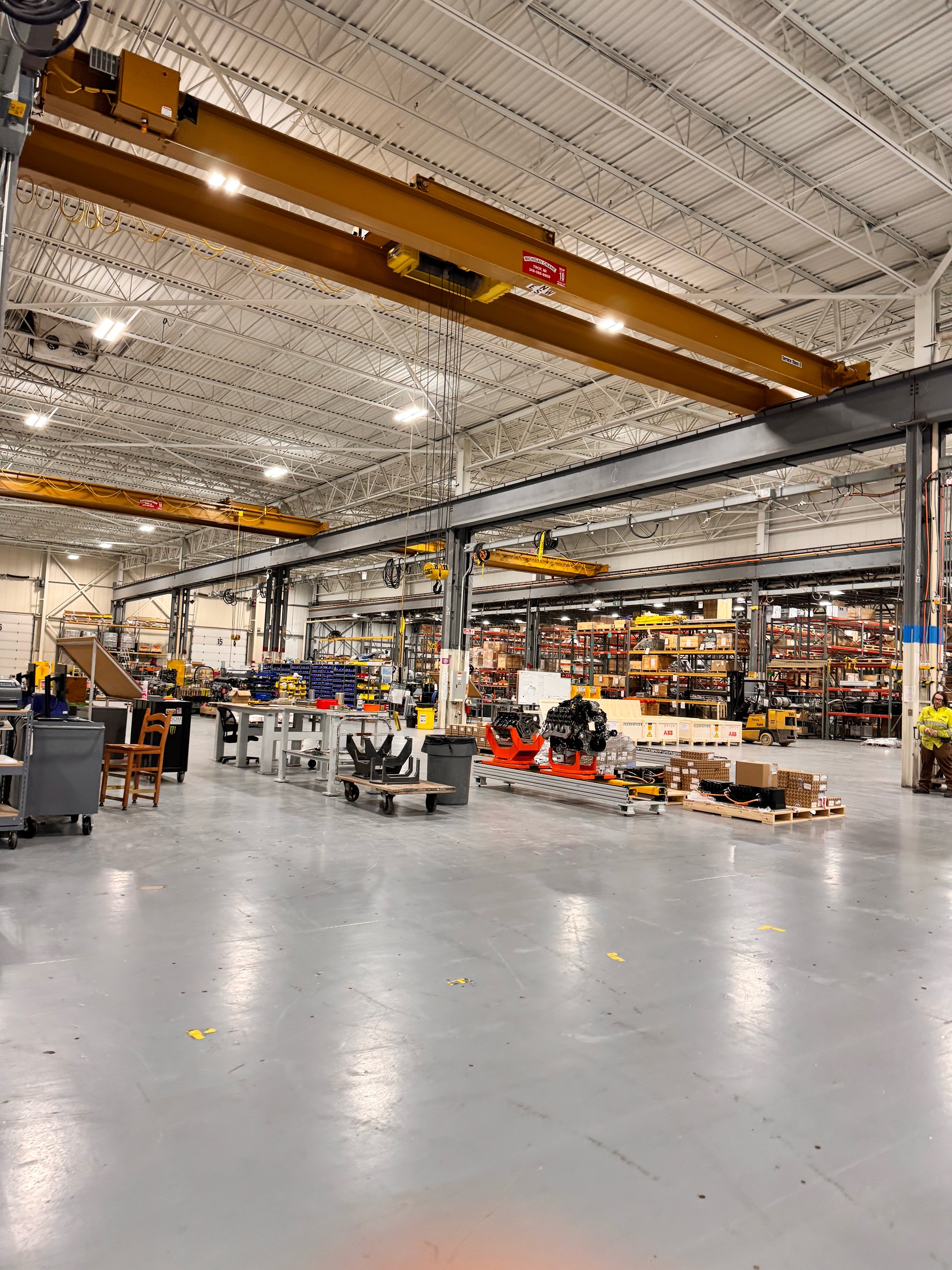 Narrow hallway with polished wooden floor, white paneled walls with hooks, closed white doors on right, and a table with wheels on the left.