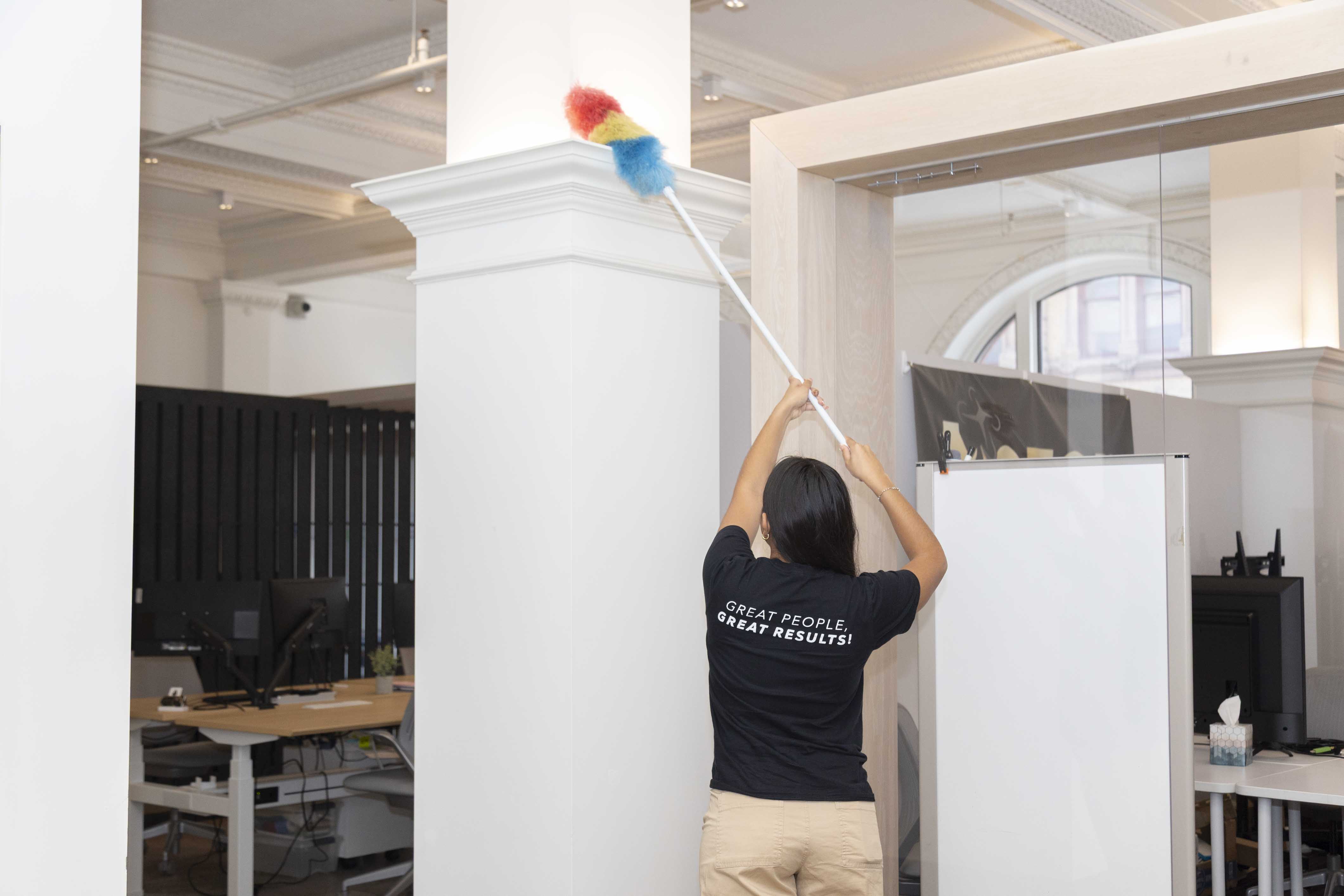 Accessible public restroom with light blue walls, wooden floor, grab bars, toilet with open seat, waste bin, paper towel dispenser, and a large wall mirror.