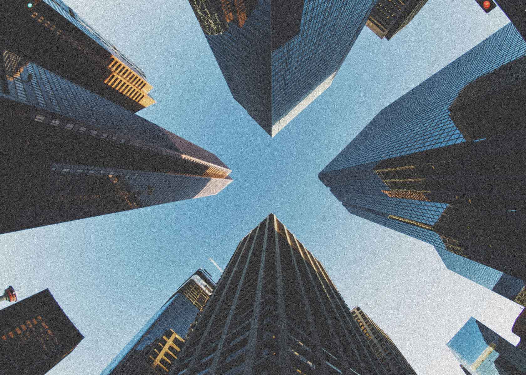 View looking up at tall skyscrapers converging against a clear blue sky in a city.