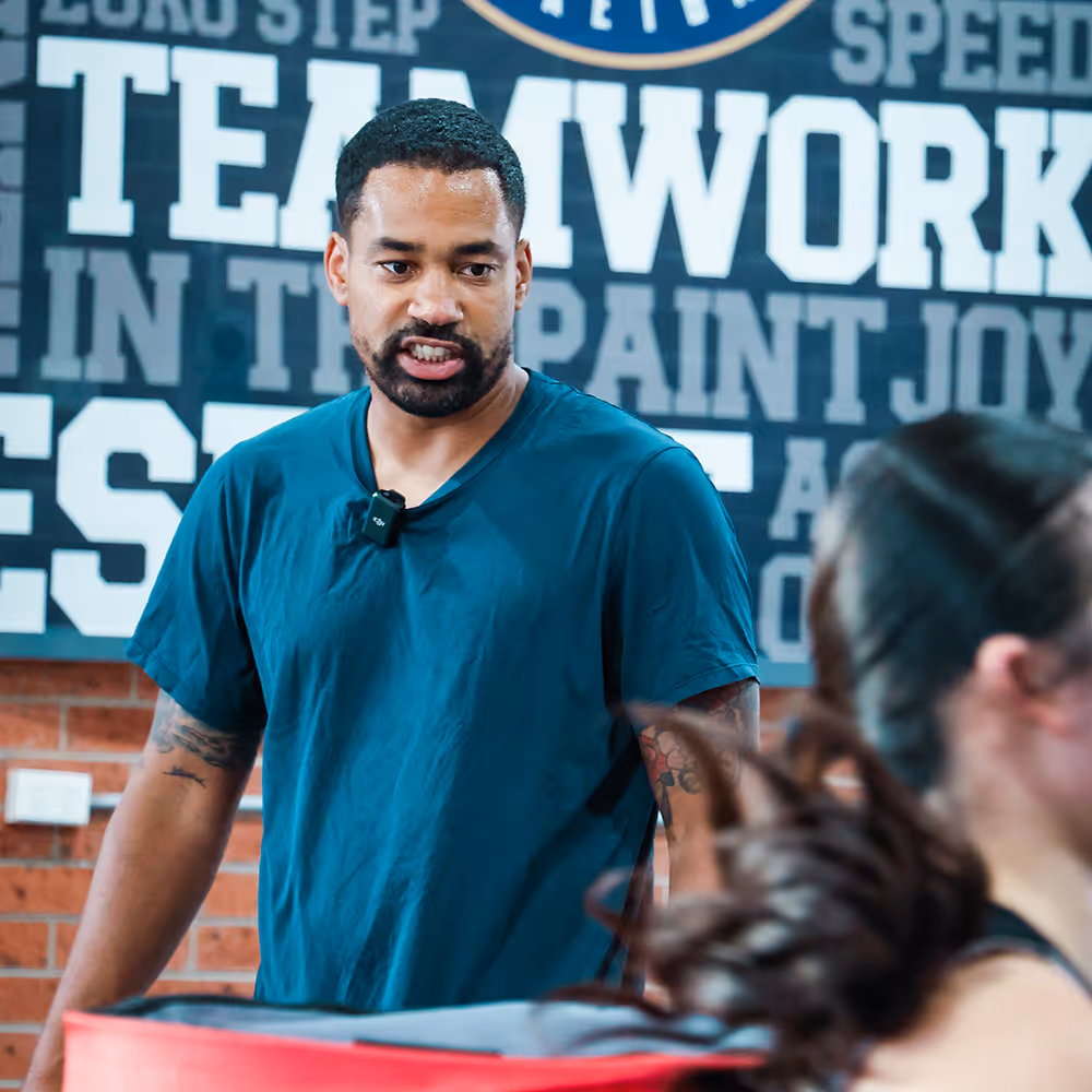 Man in teal shirt speaking with woman in gym setting with motivational teamwork text on wall.