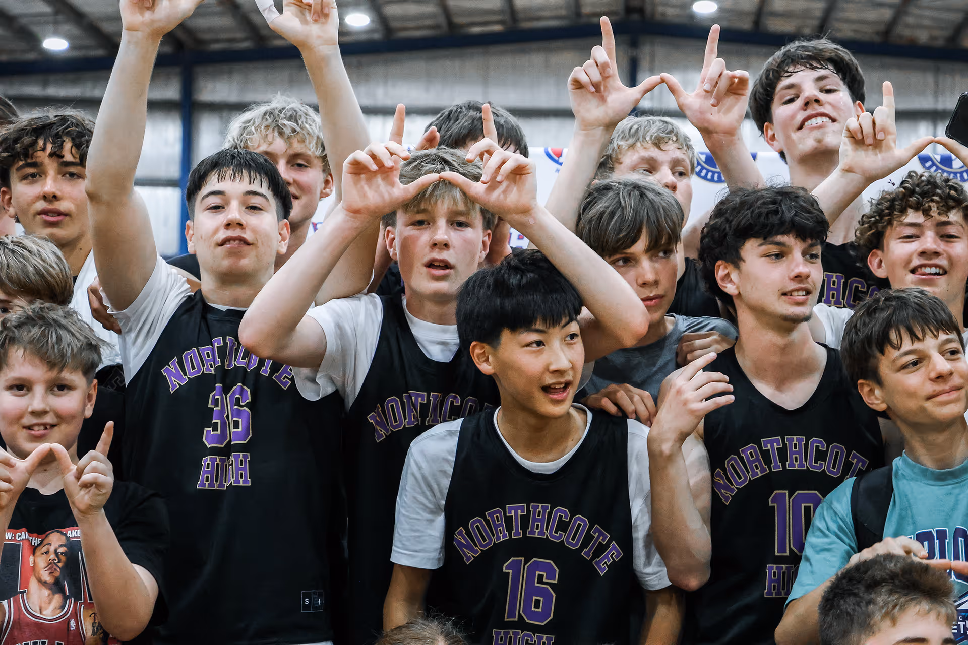 Group of teenage boys in Northcote High basketball jerseys posing indoors, some making the 'W' hand sign.