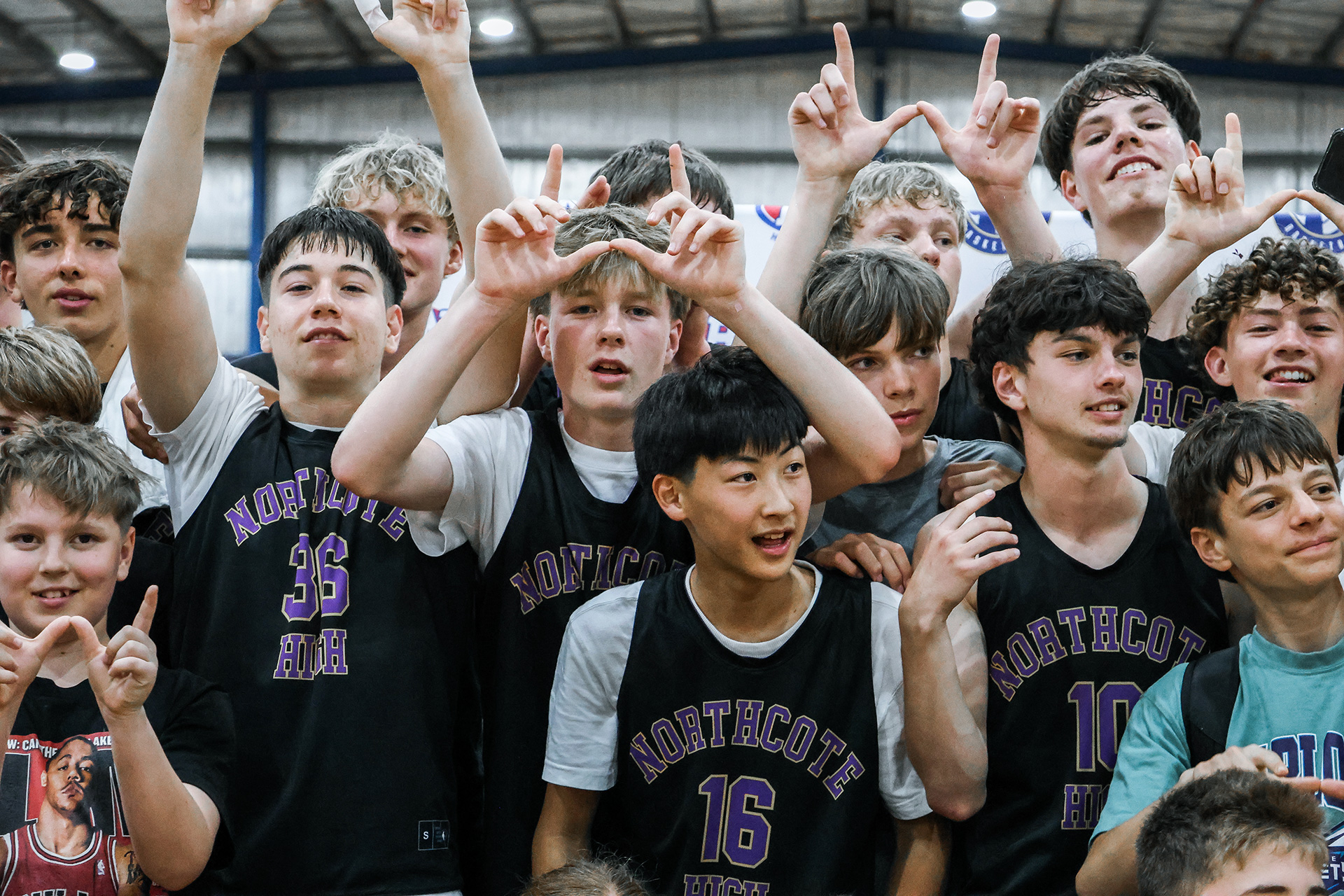 Group of teenage boys in Northcote High basketball jerseys posing indoors, some making the 'W' hand sign.