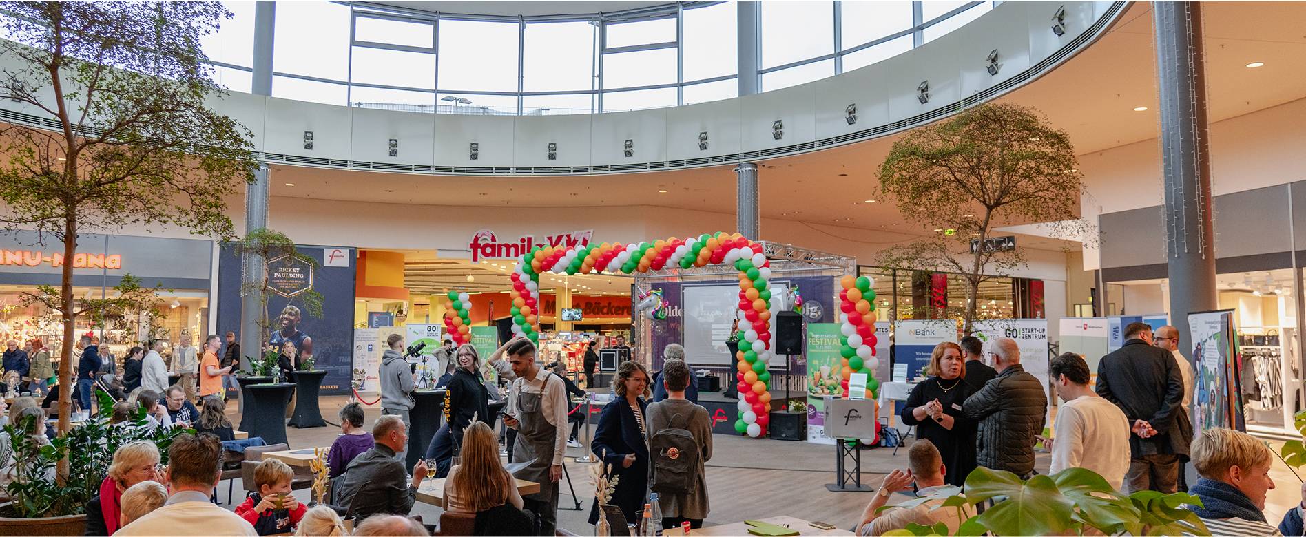 Innenaufnahme des famila Einkaufslands Wechloy mit Besuchern bei einer Veranstaltung und buntem Ballonbogen vor dem famila-Markt      