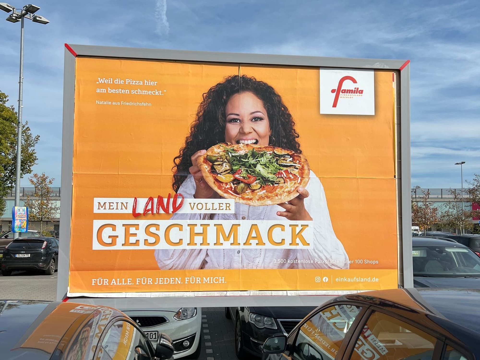 Mediafläche auf dem Parkplatz vor dem Einkaufsland zeigt eine Frau, die in eine Pizza beißt.
