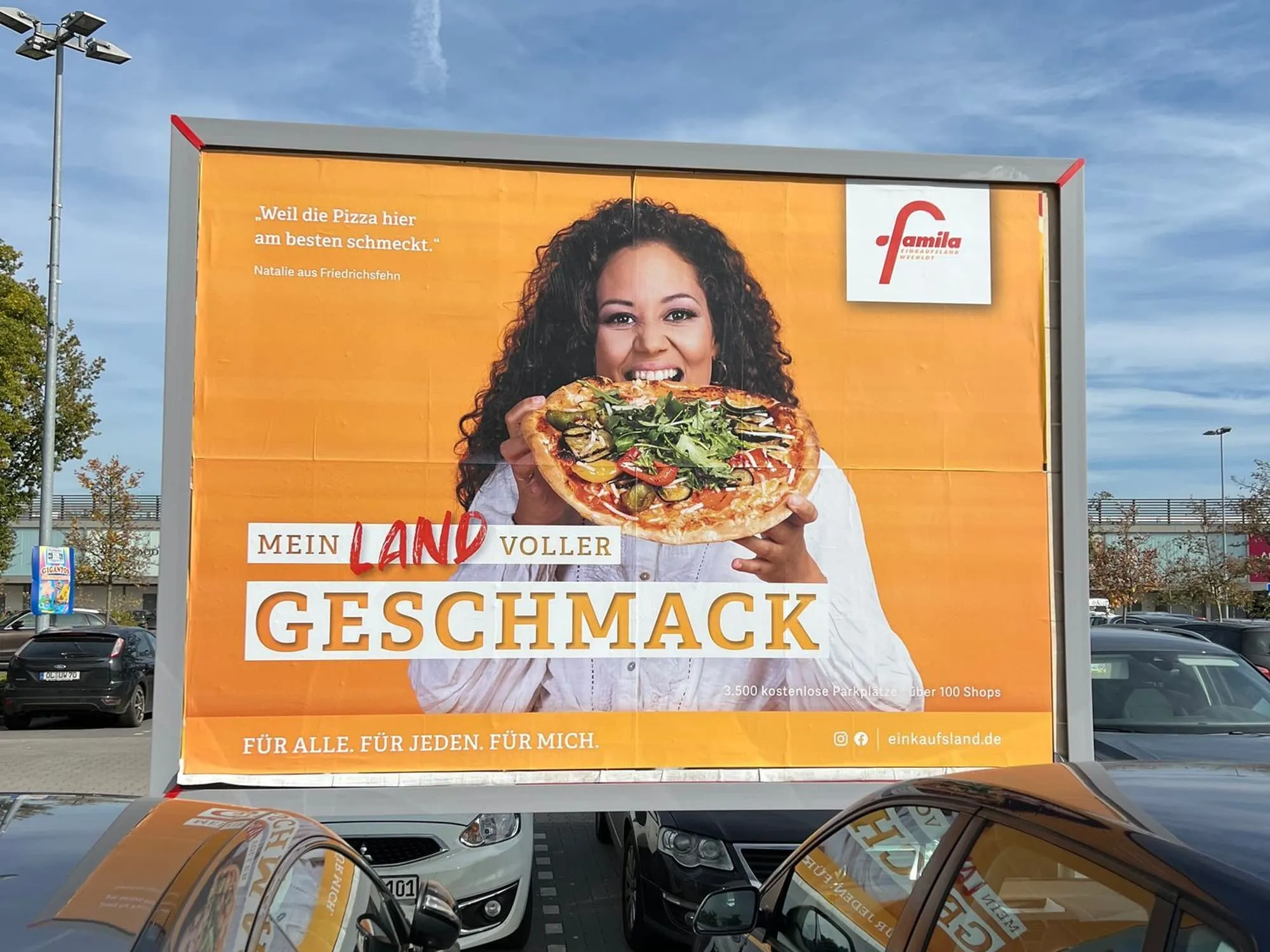 Mediafläche auf dem Parkplatz vor dem Einkaufsland zeigt eine Frau, die in eine Pizza beißt.