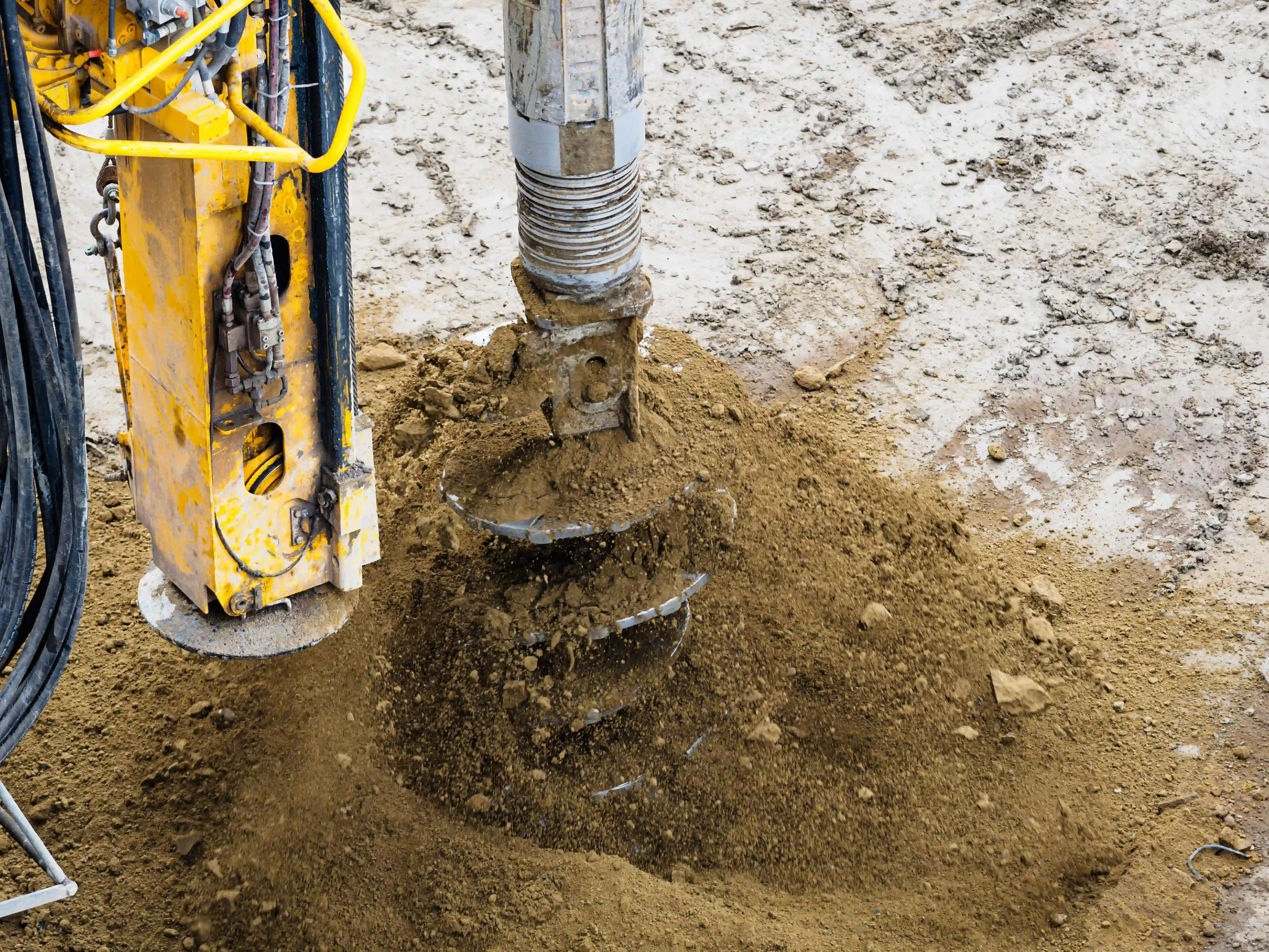 Foundation auger drilling into compacted soil on a commercial construction site