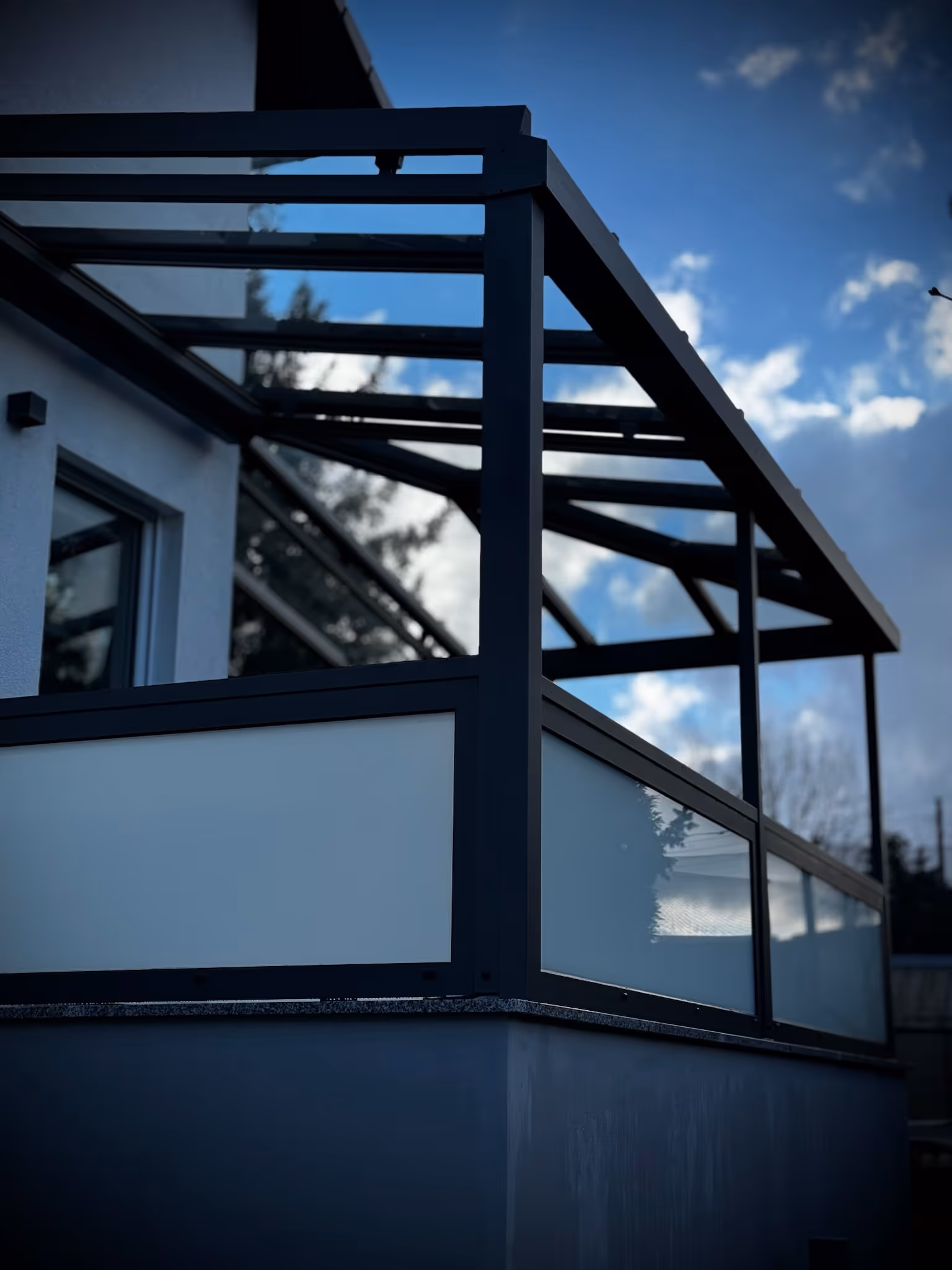 Moderne Balkonüberdachung mit einem Geländer aus Klarglas und satiniertem Sichtschutzglas.