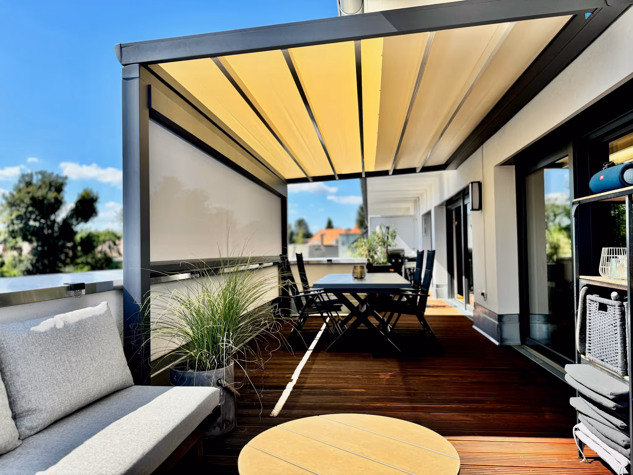 Eine Pergola-Markise mit ausgefahrenem Faltdach und seitlicher Vertikalmarkise auf einer Dachterrasse.