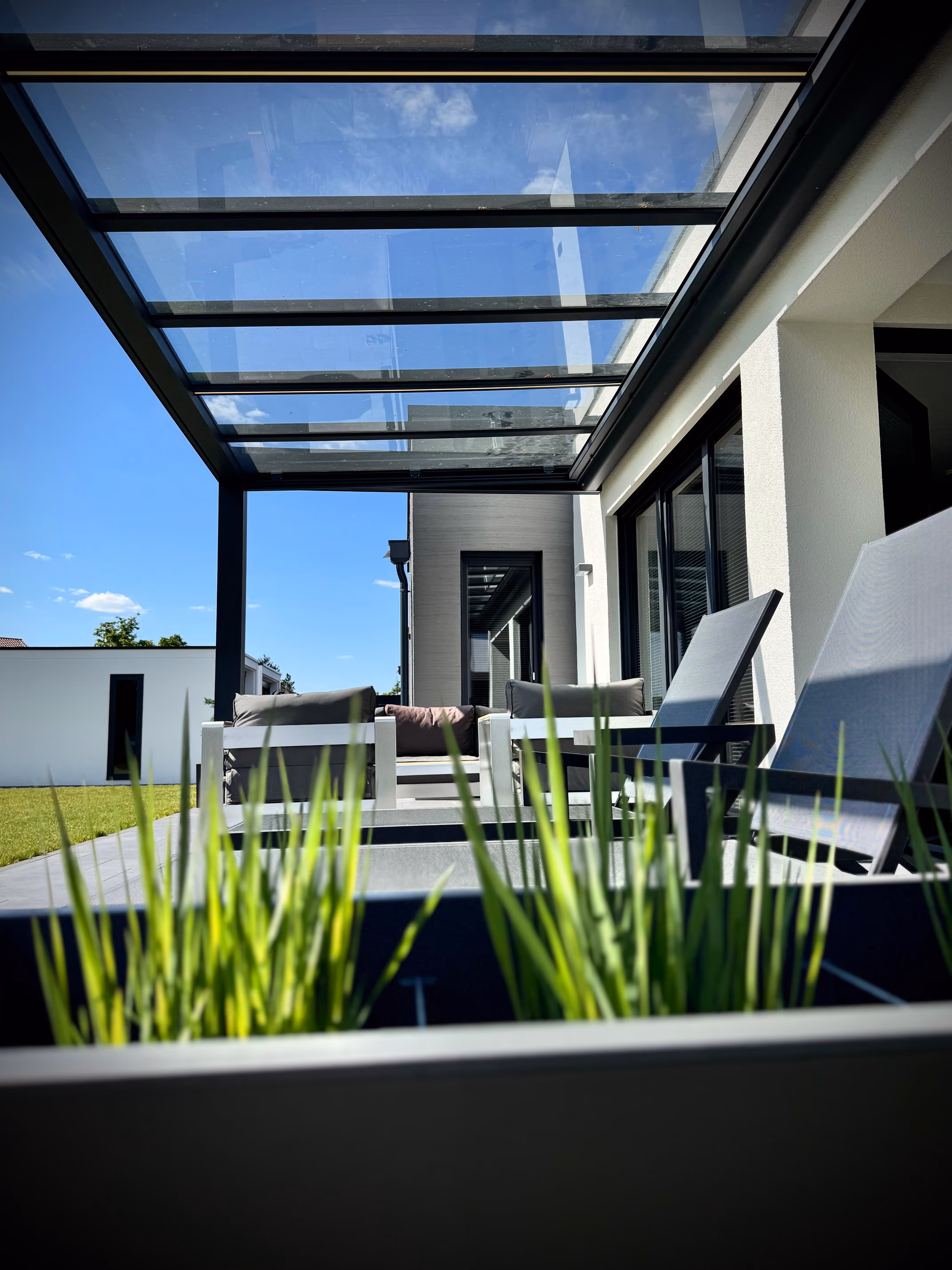 Modernes Terrassendach aus Glas schafft einen lichtdurchfluteten Loungebereich zum Entspannen.