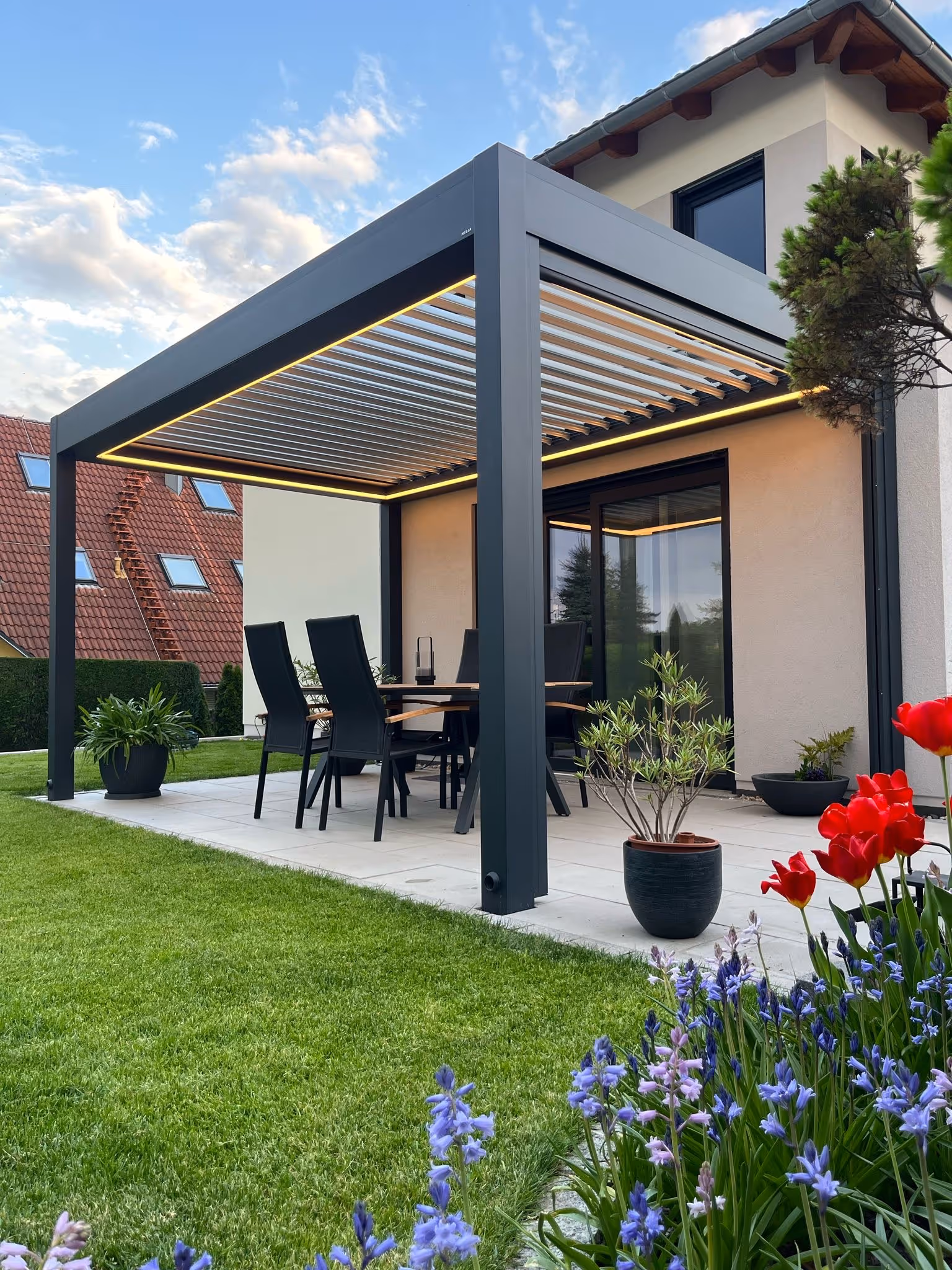  Lamellen-Pergola mit warmer Rahmenbeleuchtung als eleganter Blickfang auf der Terrasse bei Dämmerung.