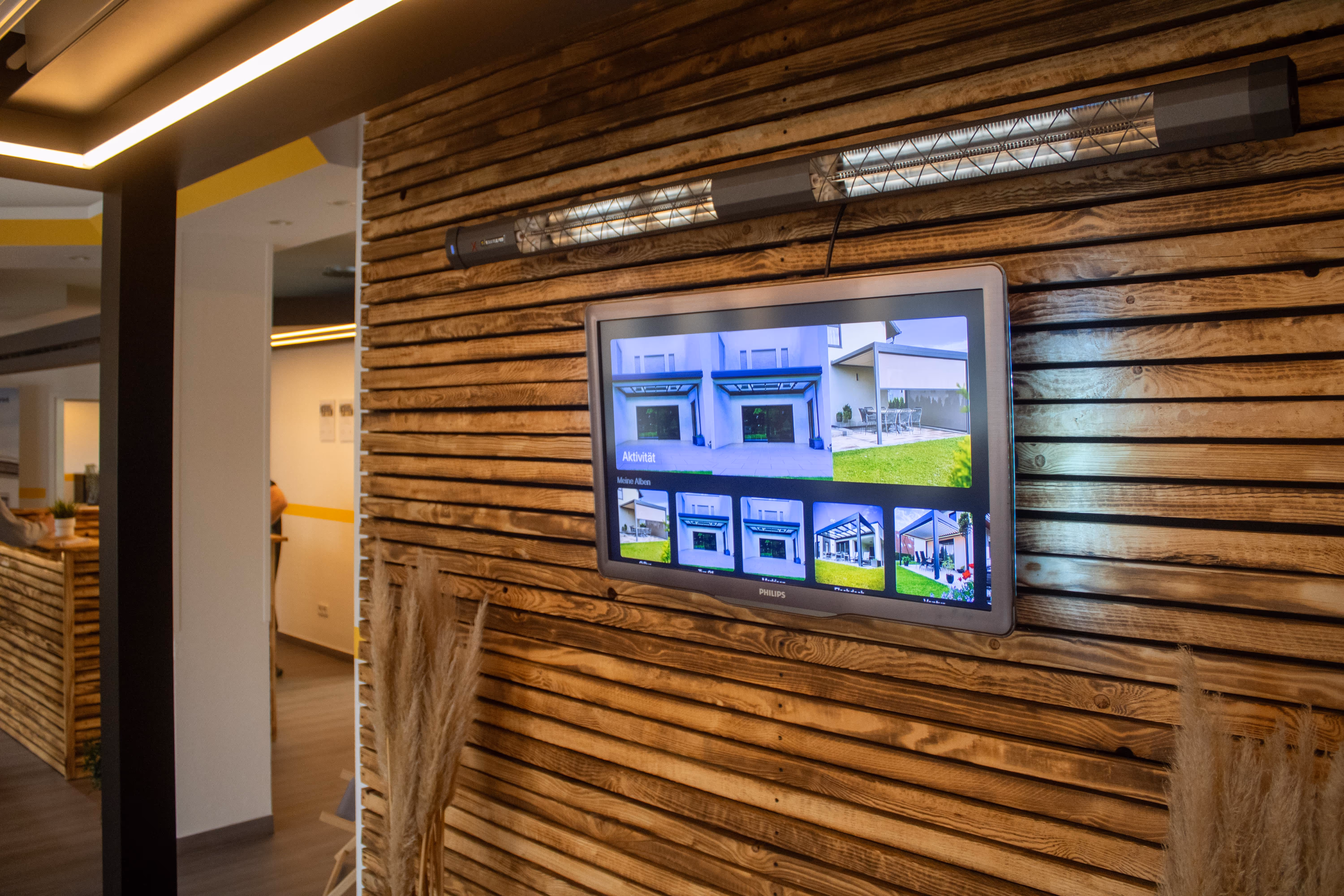 Showroom-Wand mit digitaler Projekt-Präsentation und einem darüber montierten Terrassen-Heizstrahler.