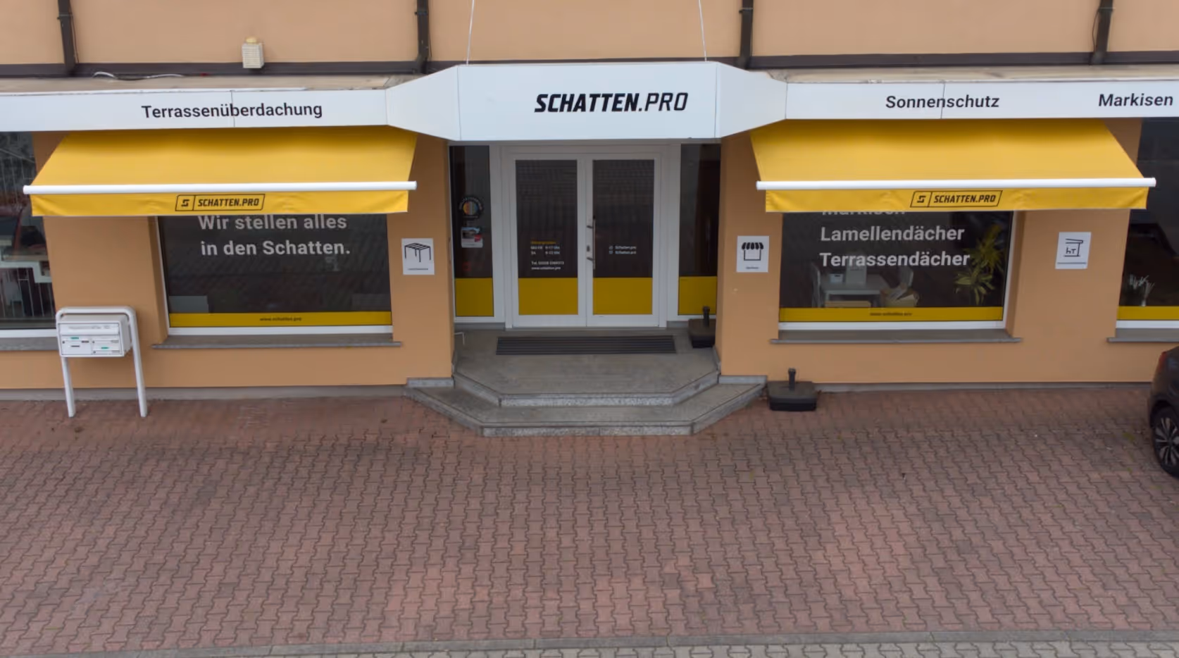 Der Eingangsbereich des SCHATTEN.PRO Showrooms mit gelben Markisen und Beschriftung für Sonnenschutz