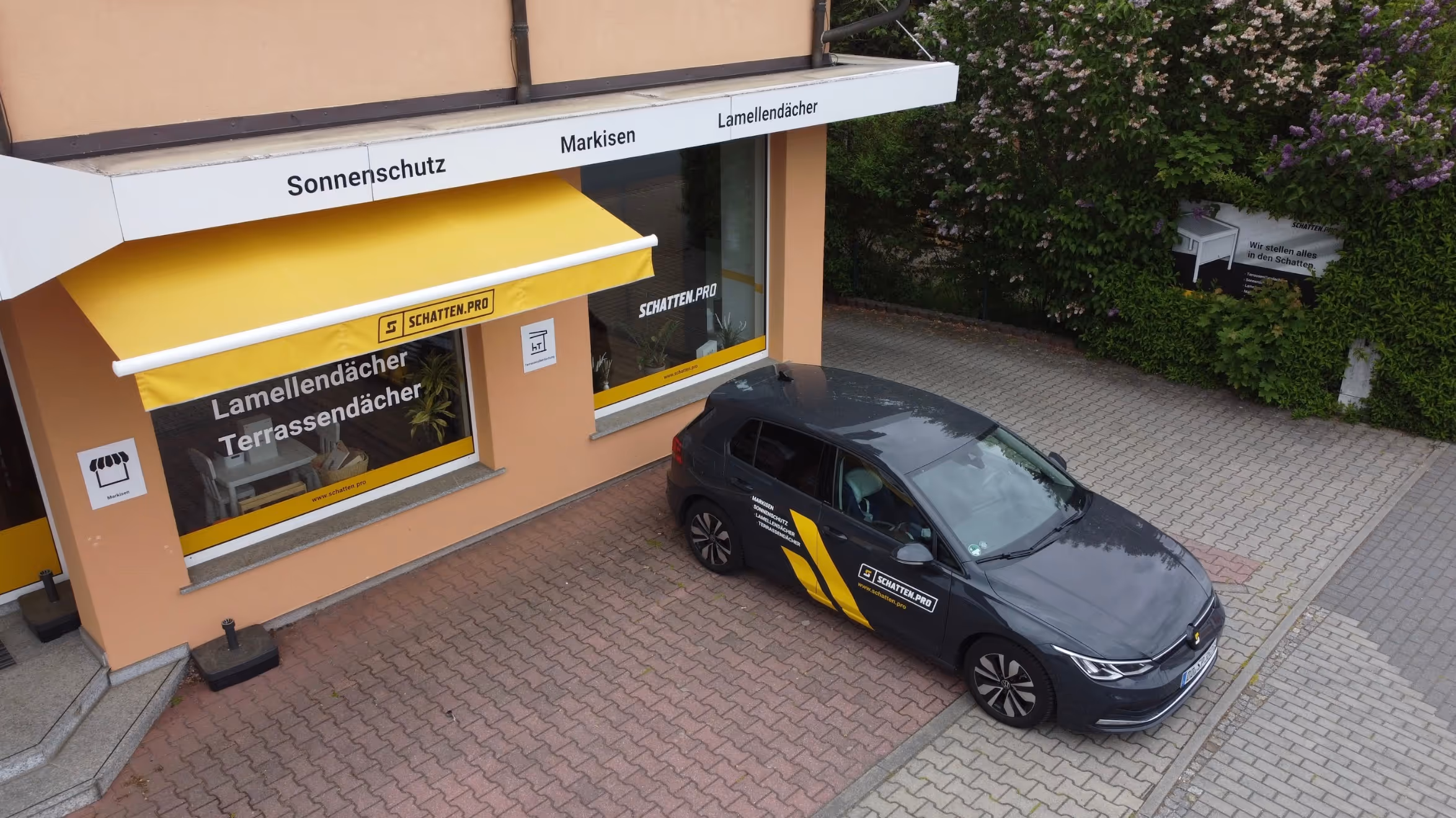 Firmengebäude mit gelber Markise, Branding „Schattenpro“ und gebrandetem Firmenfahrzeug auf dem Parkplatz