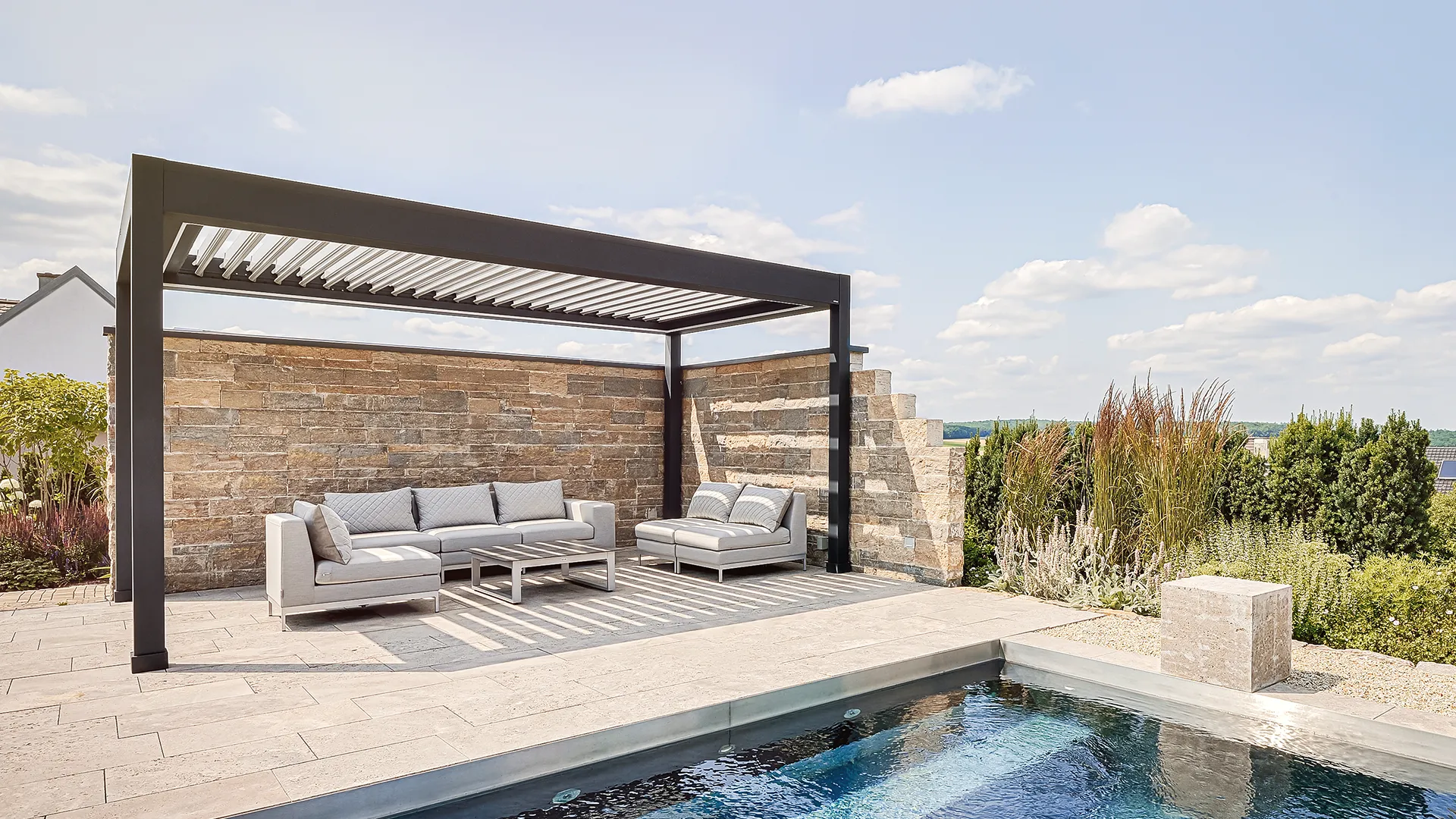 Freistehende Lamellendach-Pergola aus Aluminium als moderner Sonnenschutz für den Loungebereich am Pool.