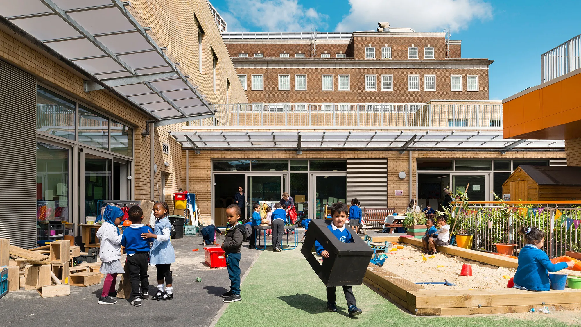 A primary school's inner playground with children playing in a sandbox and with colourful toys.