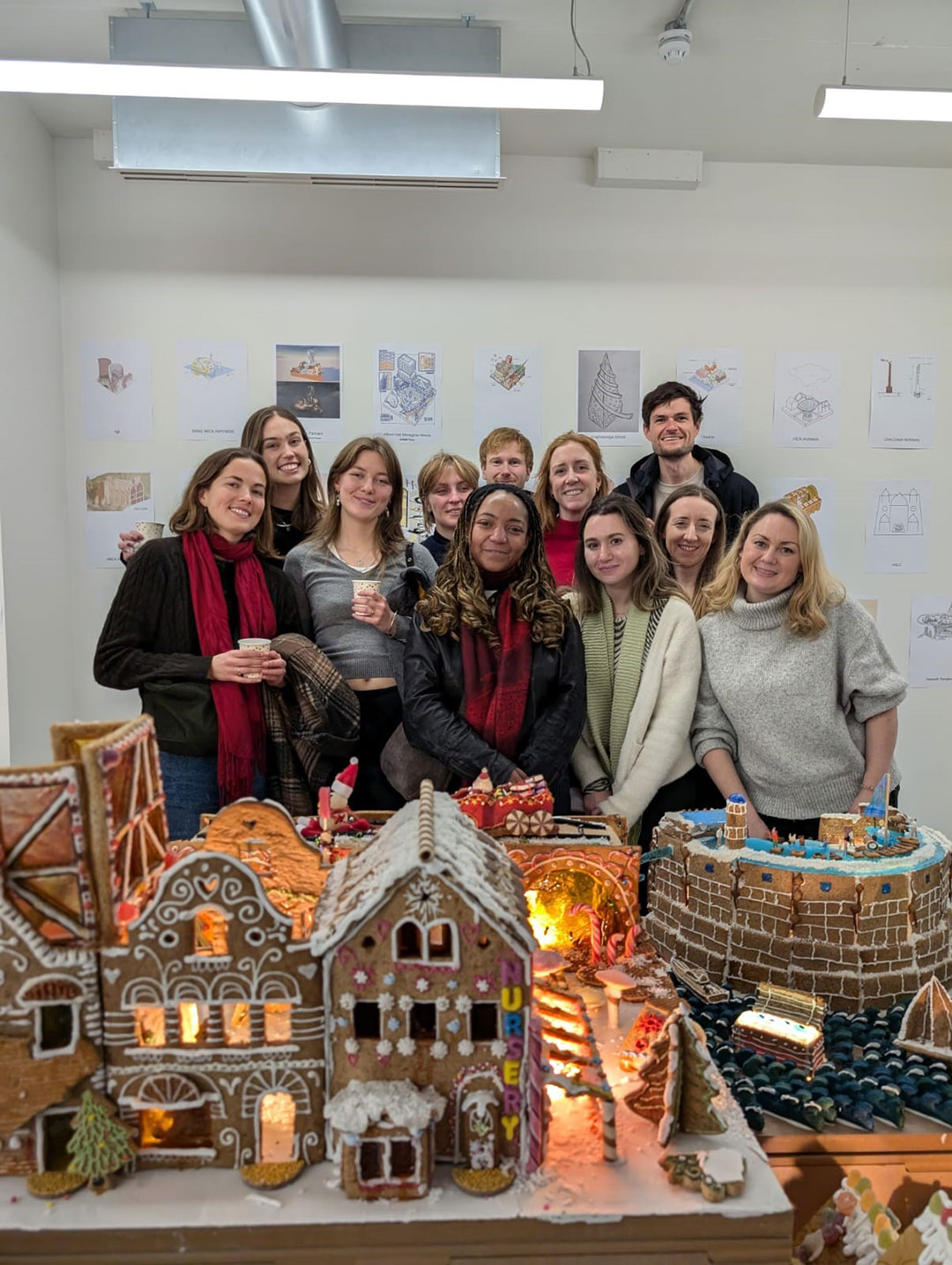 A group of people posing behind a display of Christmas gingerbread houses.