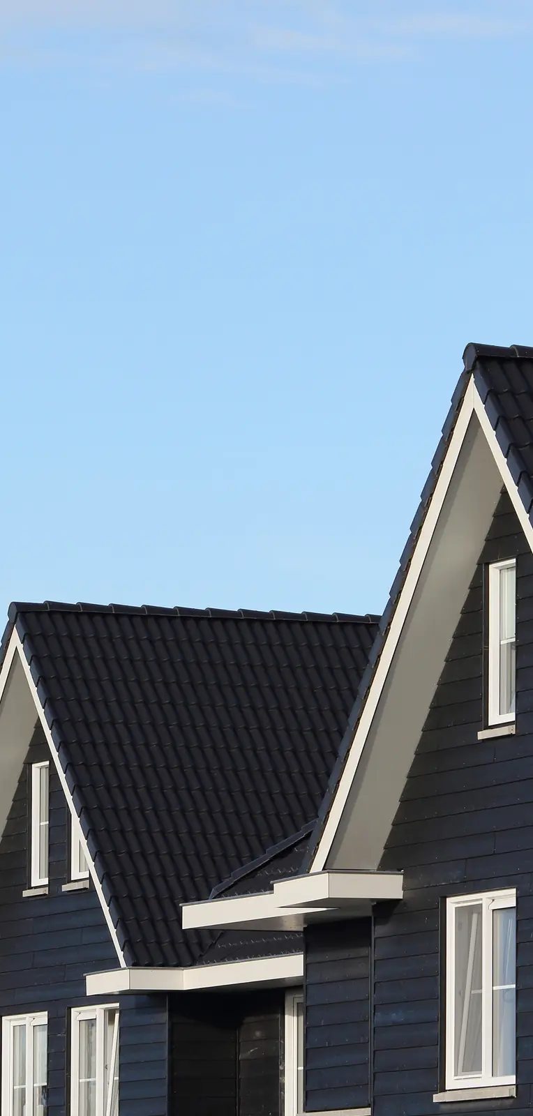 Two modern dark blue houses with white trim and steep black tiled roofs against a clear blue sky.