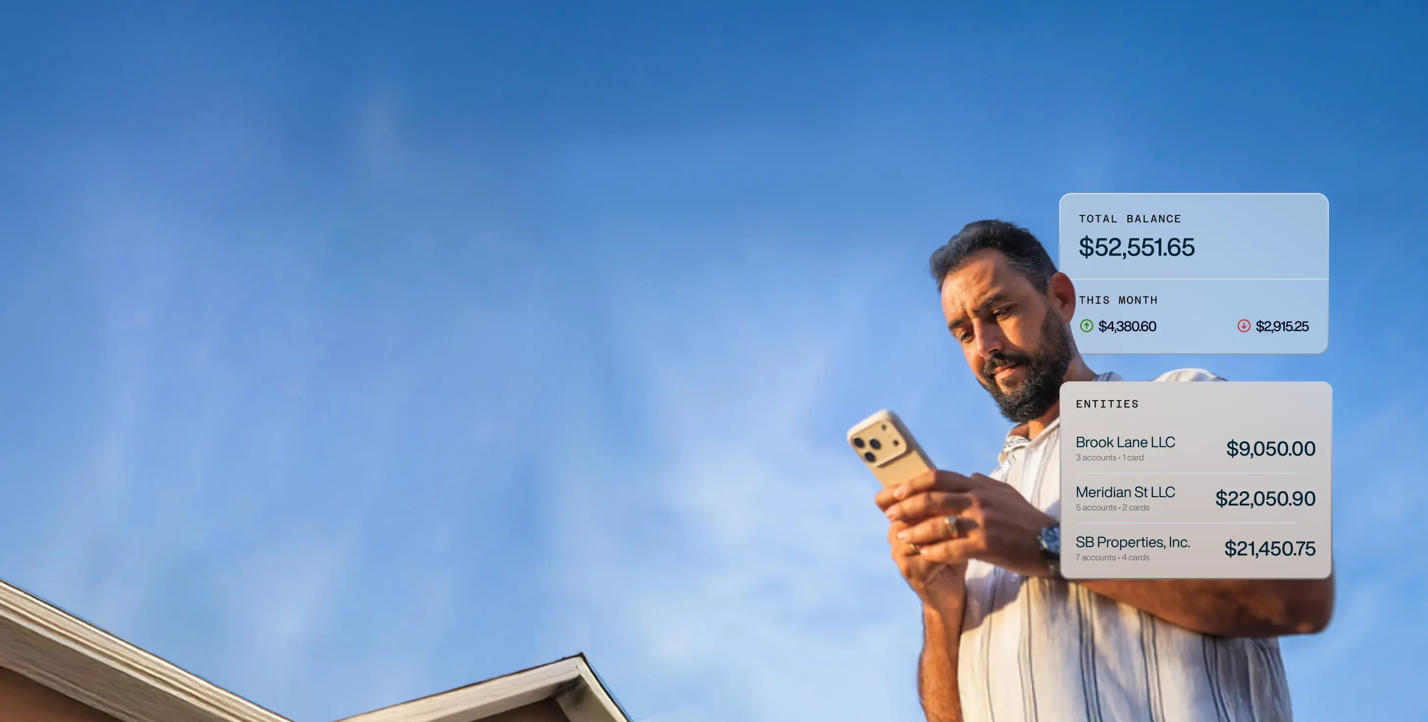 Man with beard using smartphone outdoors with blue sky background, showing banking app interface with total balance and account details.