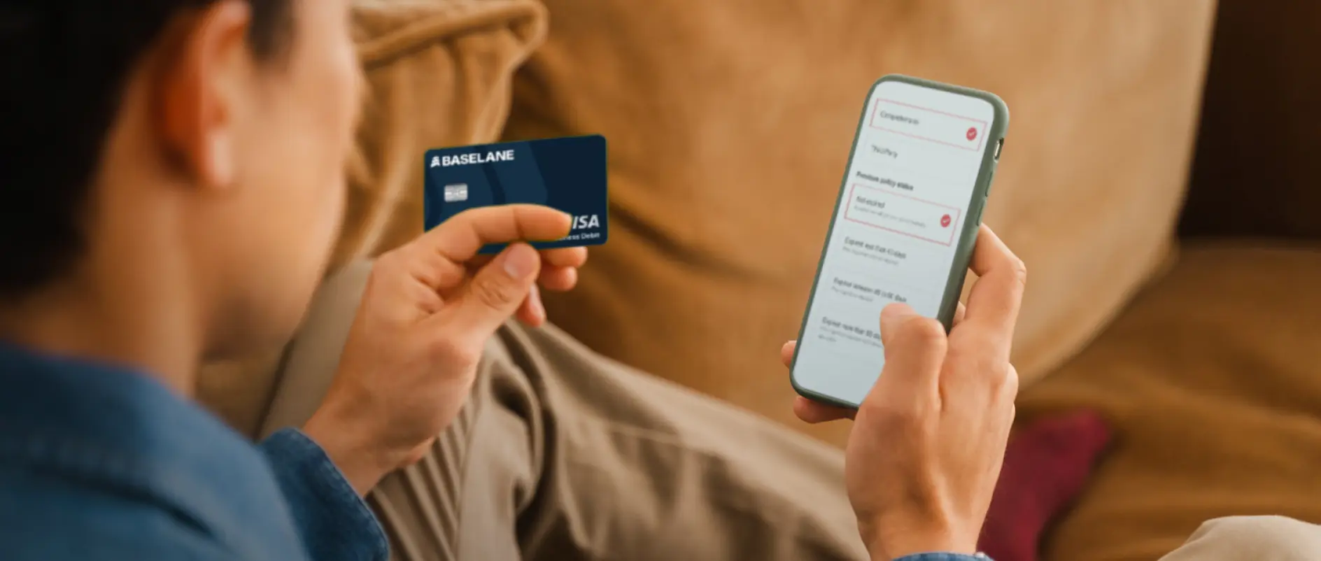 Person holding a Baseline Visa business debit card in one hand and a smartphone displaying a payment or survey app in the other hand.