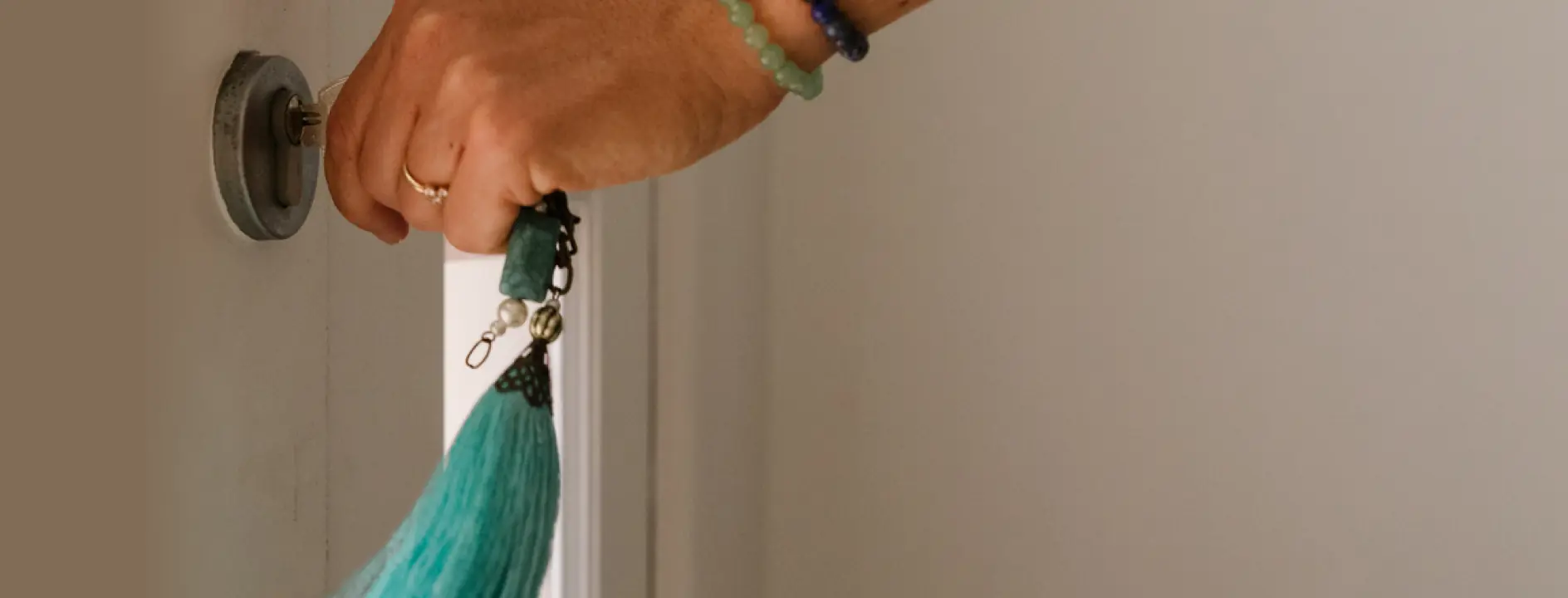 Close-up of a hand with bracelets and rings inserting a key into a door lock, holding a blue tassel keychain.