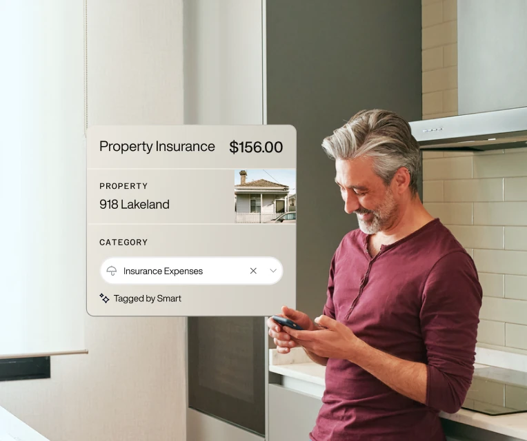 Smiling middle-aged man in a kitchen checking his smartphone with a property insurance expense overlay showing $156 for 918 Lakeland.