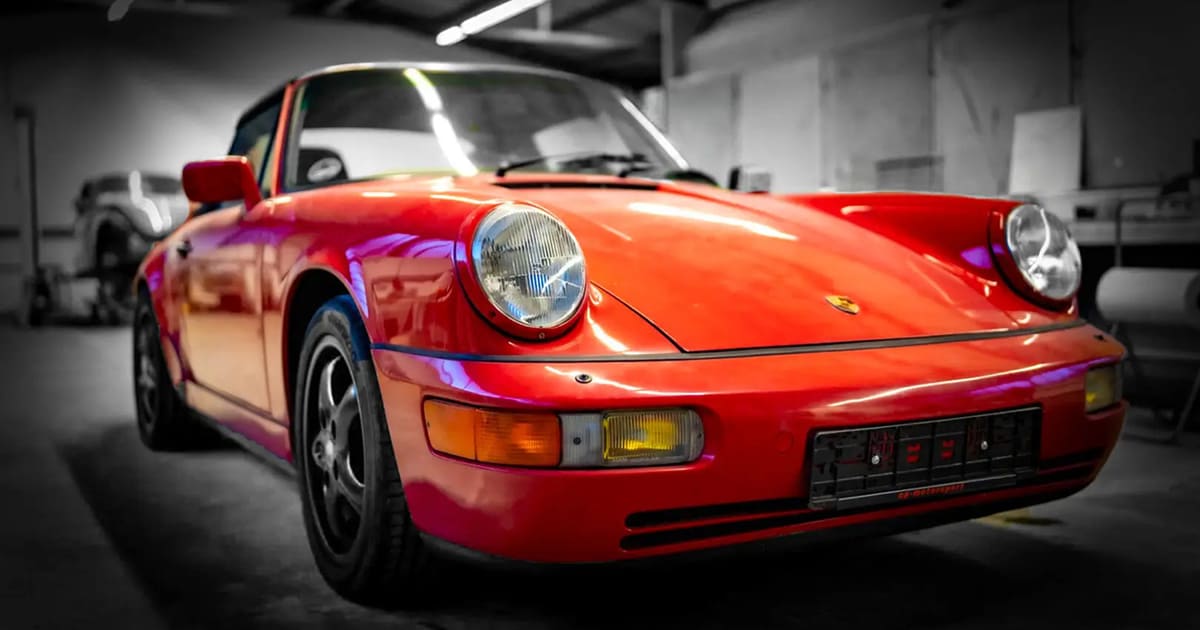 Black classic Porsche 911 parked inside an empty industrial warehouse.