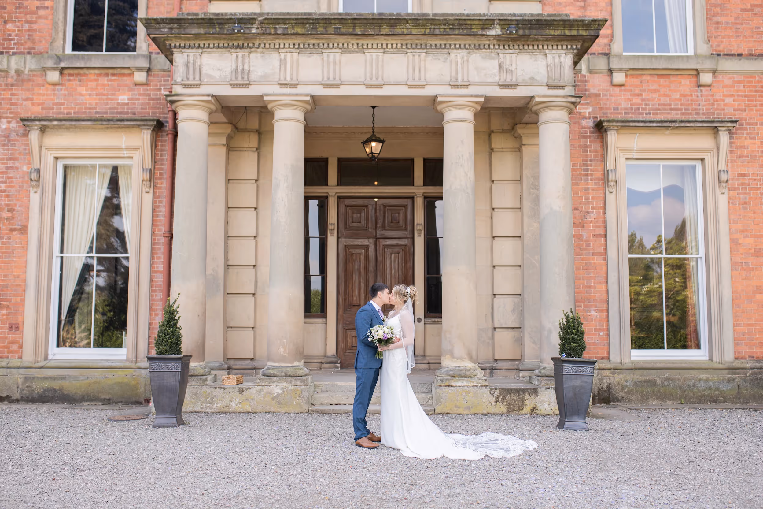 Bride and groom embracing in front of hall entrance.