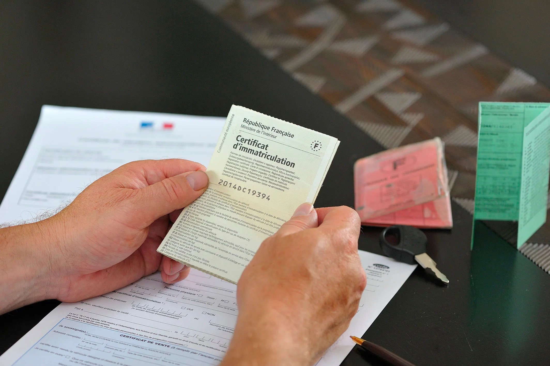 Mains tenant une carte d’identité et un permis de conduire, illustrant l’usurpation de documents d’identité officiels: carte de certificat d'immatriculation et sur la table on peut voir un permis de conduire une contravention.