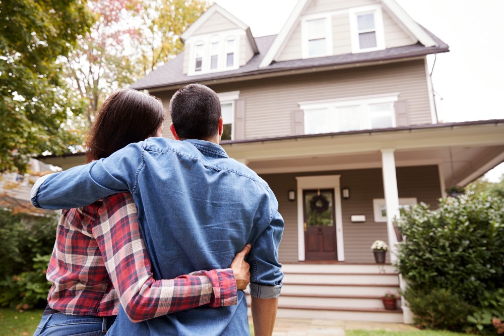 Couple embraces and looks at their home from the front yard