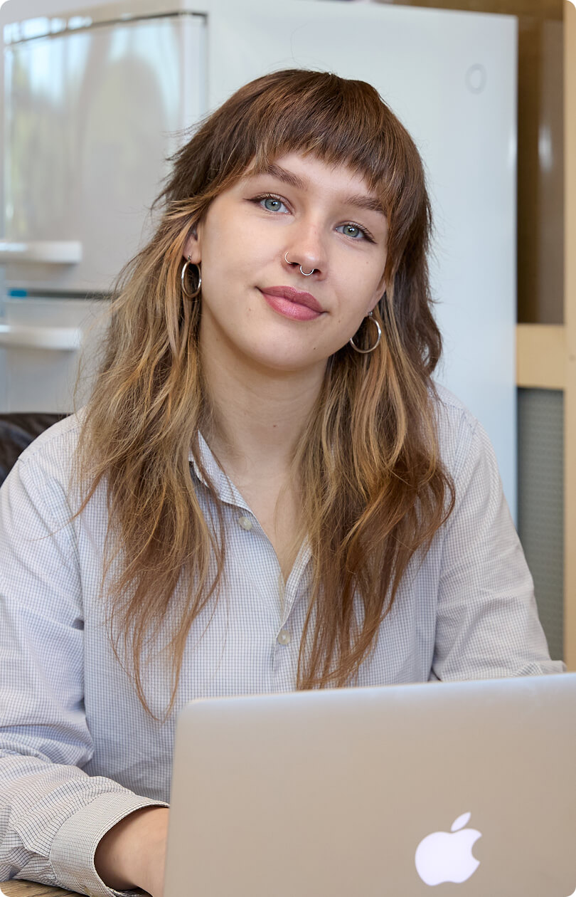 Jonge vrouw met neuspiercing werkt aan MacBook in kantooromgeving