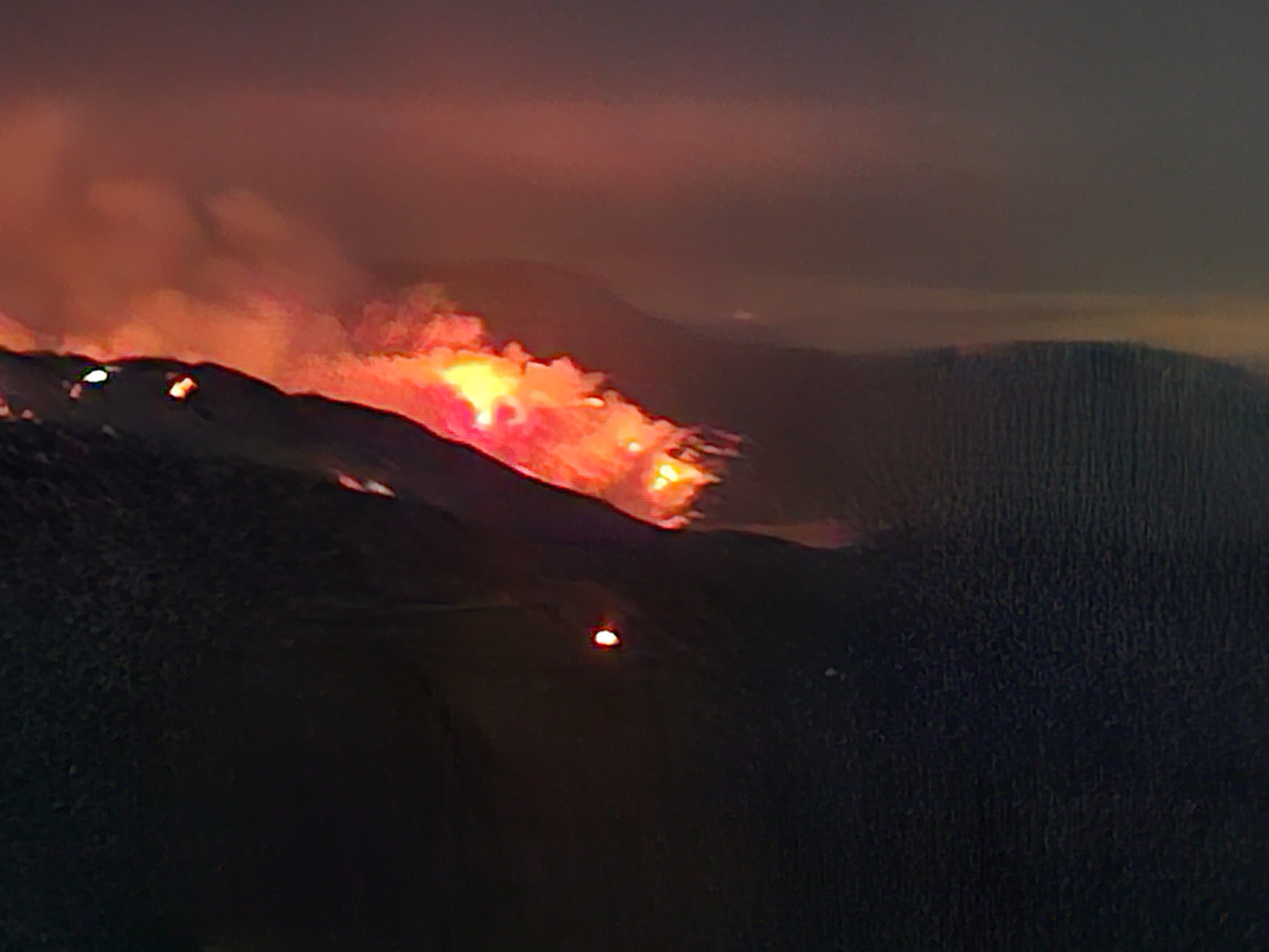 Wildfire on dark mountain with smoke and clouds in sky and red flames.
