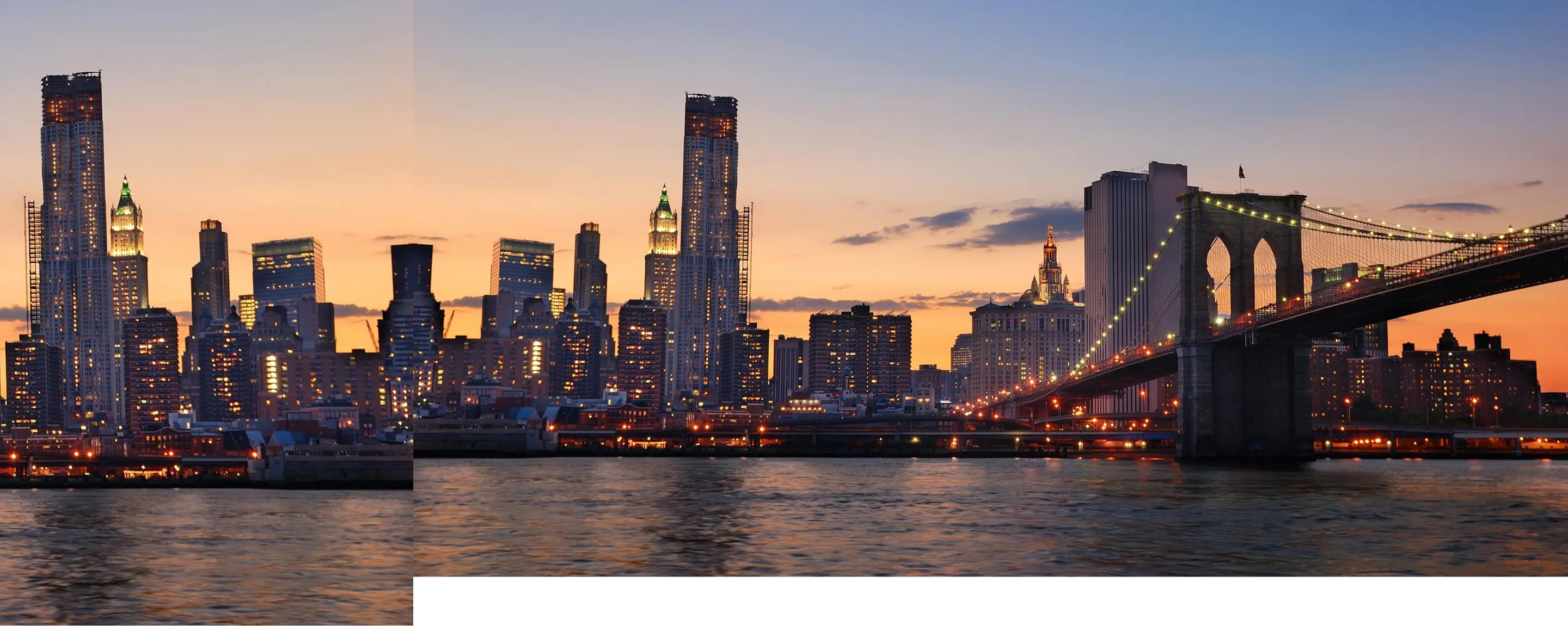 Brooklyn Bridge and lit Manhattan skyline at sunset over the East River in New York City.
