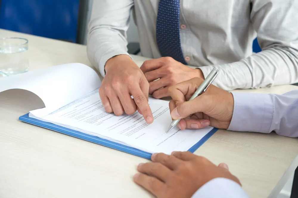 Two people reviewing a document while one points and the other signs with a pen on a white table.